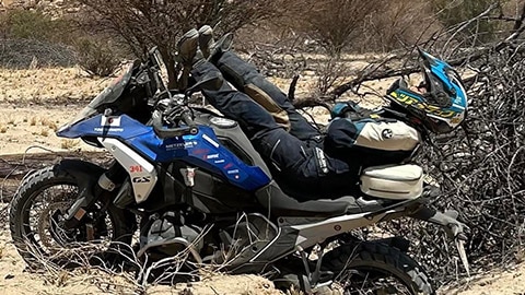 Zawodniczka z japońskiej drużyny kobiet leży na motocyklu R 1300 GS. Jej nogi są ułożone w stronę kierownicy, a ramiona i głowa wystają ponad tył motocykla.